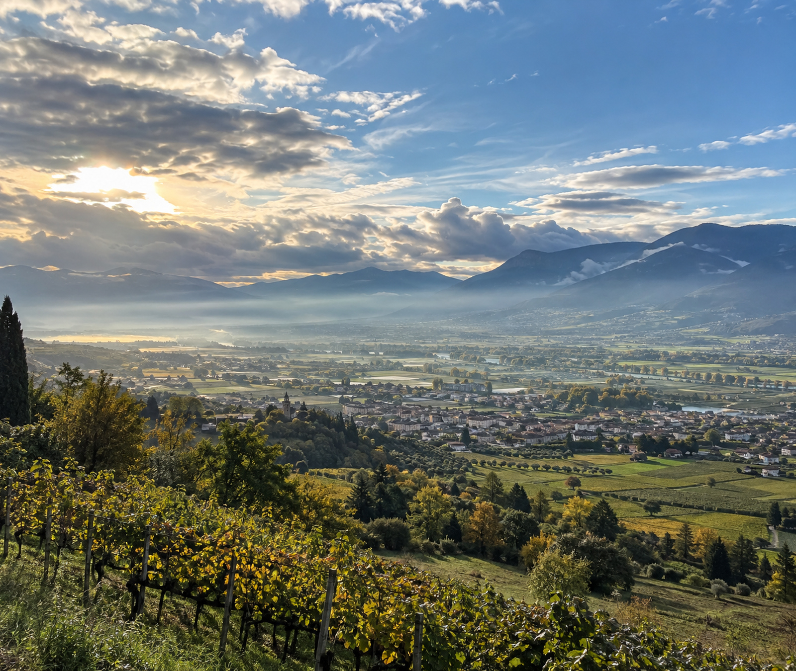 Paesaggio italiano di inizio autunno con sole, vigneti e nuvole più dense sulle montagne