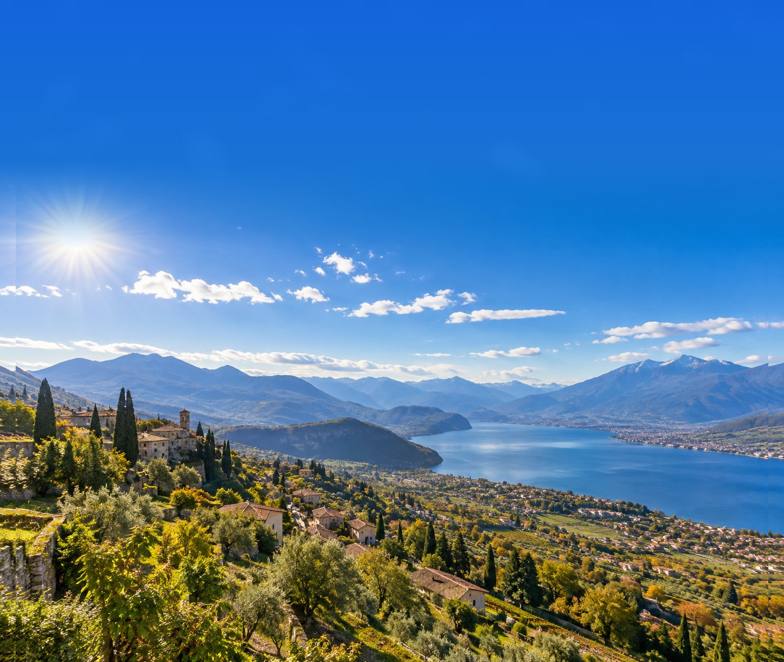 Paesaggio italiano soleggiato di fine settembre con lago, colline, ulivi e montagne.