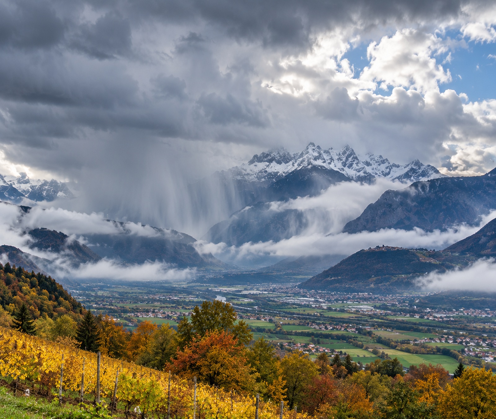 Immagine simbolica: paesaggio autunnale dell’Italia settentrionale con rovesci, nubi basse e Alpi sullo sfondo.